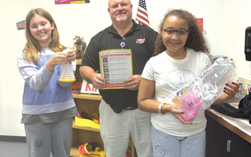 Charlie Stermer (from left) holds a LifeVac Airway Clearance Device while  standing with Ed Carter, Fort White Elementary School principal, and Aubrie Brown, holds a bag with another of the devices. (COURTESY)