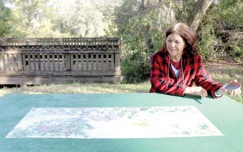 Local artist Judith McClure looks over a piece she created on a picnic table in Way Side Park in White Springs. The Our Community Cares Coalition, adults, youth members and community volunteers are creating a mural at the park’s boat ramp to go along with adding images to picnic tables at the park. (TONY BRITT/Lake City Reporter)