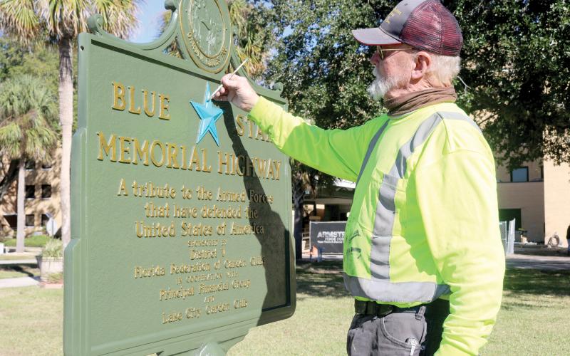 Thomas L. Stelling with Historical Markers Restorations paints the blue star on the Blue Star Memorial Highway marker that sits in front of the Lake City VA Hospital. Stelling restored the sign last week for the Lake City Garden Club. (TONY BRITT/Lake City Reporter)
