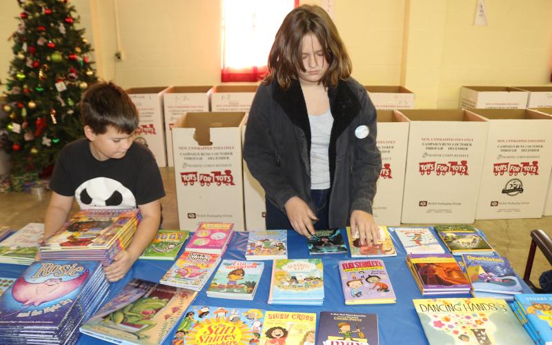 Phury Hunlock (left), 10, and Piper Hunlock, 13, volunteer their time arranging books that will be given as Toys for Tots Christmas gifts. (TONY BRITT/Lake City Reporter)