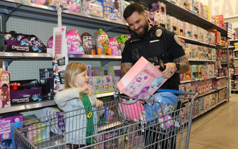 Kylin Barwick, 7, gets a smile from Lake City police officer Kevin Johnson as she tells him about a toy she plans to purchase during the Shop With A Cop event on Wednesday morning at Walmart. (TONY BRITT/Lake City Reporter)