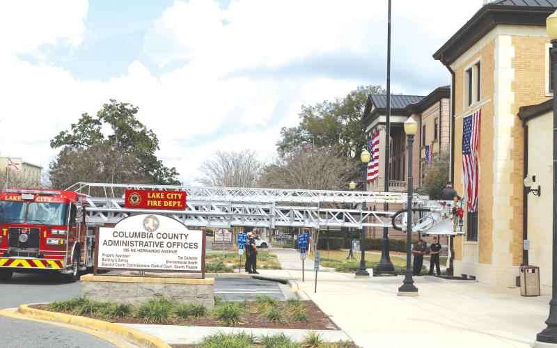 Lake City Fire Department firefighters use their Tower 1 truck to hang the American Flag on the Columbia County Commission Annex Building on Saturday morning. (TONY BRITT/Lake City Reporter)