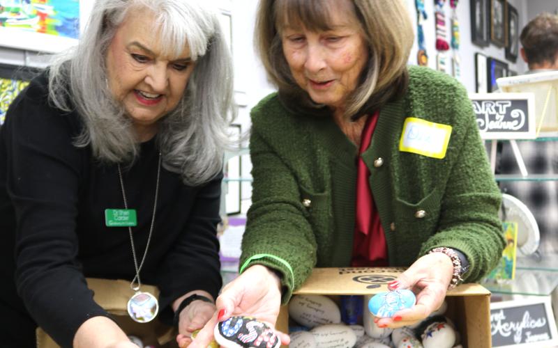 Sheri Carder (left) and Dee Etheridge have fun and share laughs while they go through a box of Freedom Rocks at the Gateway Art Gallery last month. (TONY BRITT/Lake City Reporter)