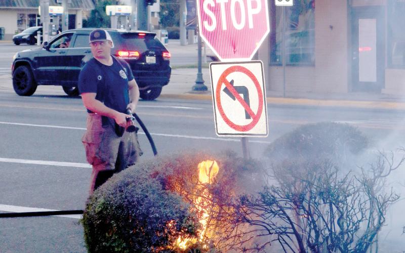 Lake City firefighter Josh Morris, uses a small hose as he prepares to extinguish shrubbery that caught fire near the Columbia County Courthouse Annex on Wednesday evening. (TONY BRITT/Lake City Reporter)