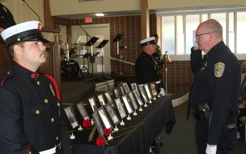 Lake City police officer Greg Burnsed salutes pictures of fallen first responders after placing a flower in honor of them at last year’s Public Safety Memorial. (FILE)