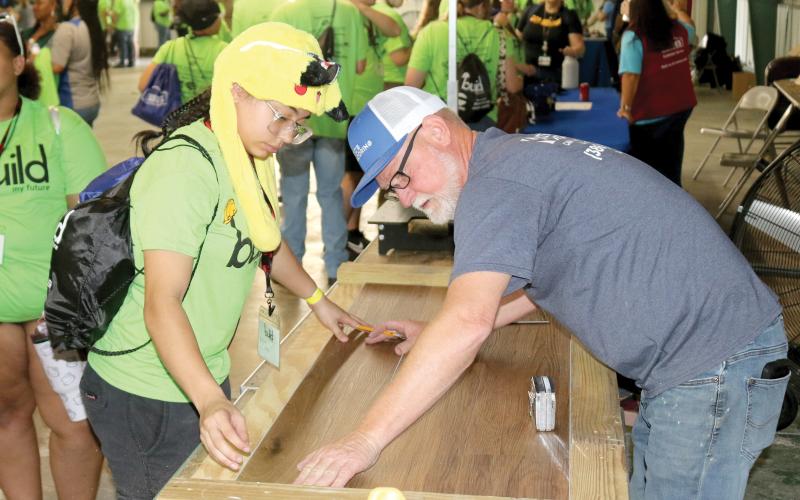 Maylianne Vazquez (left) works on connecting pieces of flooring with Eric Adams of Eric’s Flooring during Wednesday’s Build My Future event. (TONY BRITT/Lake City Reporter)