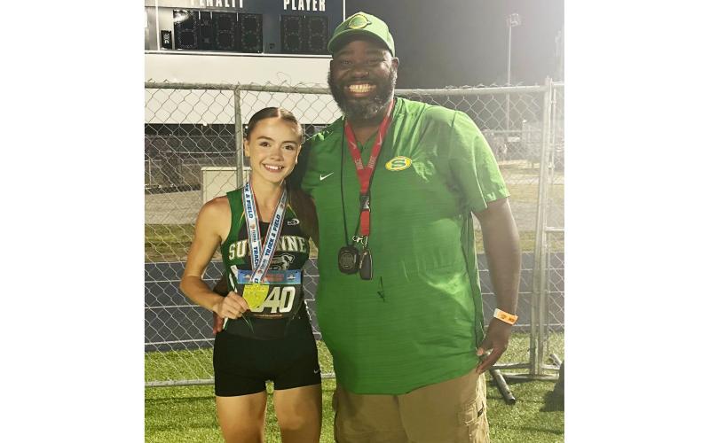 Suwannee senior Ryleigh Hermanson shows off her Class 2A state championship medal in the 1600m alongside assistant coach Twon Williams on Thursday. (COURTESY)