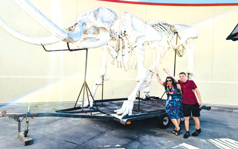 A couple of people pose under the replica mastadon skeleton that was on display at the Columbia County Public Library during a summer kickoff event on Friday. (COURTESY)
