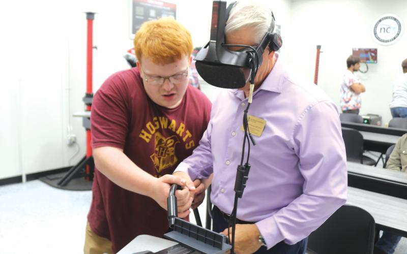 Brody Hoffman (left), a Florida Gateway College student, helps Mitchell Maione, a coordinator for the FGC physical therapy program, as Maione uses a VR welding simulator during the college’s grand opening for its newly renovated welding technology program on Tuesday afternoon. (TONY BRITT/Lake City Reporter)