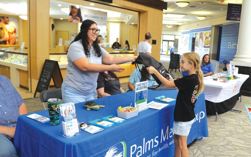 Vivian Jones (from left) of Palms Medical Group gives a book bag to Erin Neal, 10, at the Lake City Mall on Saturday during the Movin’ and Groovin’ Back to School event. (TONY BRITT/Lake City Reporter)