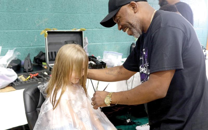 Lilly Miles, 6, gets a face frame and trim from local barber Tyrone Mullins during the Community Barbers Back-to-School Bash at the Richardson Community Center on Sunday. More than 1,000 people attended the event. (TONY BRITT/Lake City Reporter)