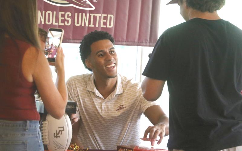 Former Florida State quarterback Jordan Travis smiles as he signs Kyler Keen's box of Cheez-Its during a meet-and-greet at the Country Club at Lake City on Thursday. (MORGAN MCMULLEN/Lake City Reporter)