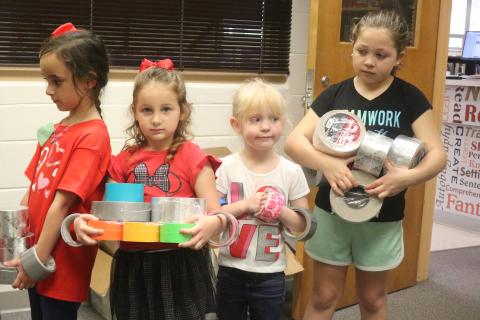 Eastside Elementary School students Ryleigh Trespalacios (from left), Aunna Hartopp, Summer Bedenbaugh and Ariana French bring rolls of duct tape to the school library Thursday morning. The school hopes to set a world record for the largest ball of tape. (TONY BRITT/Lake City Reporter)