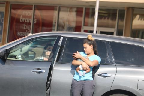The woman authorities say left a baby unattended in a car Monday afternoon sits in the vehicle at Lake City Plaza as the baby’s mother holds the child. (TONY BRITT/Lake City Reporter)