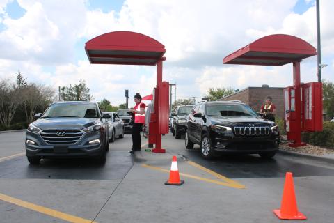 Chick-fil-A employees take orders and payment from customers Wednesday afternoon as patrons form a line in their vehicles. The eatery is not allowing customers in its dining room and only providing drive through services because of the COVID-19 global pandemic. (TONY BRITT/Lake City Reporter)