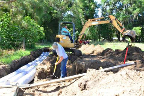 Charles Peloni, owner of Peloni’s Pumping and Portable Toilets, pictured on the right operating heavy machinery, installs a new septic tank with his employee and stepson, Joseph Creeley, pictured on the left. Peloni says business has slowed down in some aspects but picked up in others during the pandemic, resulting in revenue staying steady. (CARL MCKINNEY/Lake City Reporter)