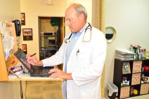 Local physician Peter Giebeig, who practices family medicine, performs administrative work at a computer station in his practice. Giebeig says the pandemic has cut business in half due to patients being more cautious about where they go in public. (CARL MCKINNEY/Lake City Reporter)
