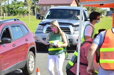 A health official directs traffic during a drive-thru covid-19 testing event Tuesday morning at Wilson Park by Lake DeSoto. CENTER: Workers from the Florida Department of Health suit up to begin testing. (CARL MCKINNEY/Lake City Reporter)