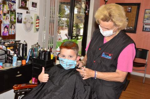 Louise Huelskamp, better known as “Miss Wezzie,” puts the finishing touches on 8-year-old Hagan Stalvey, who also asked for a touch of pink coloring in his hair.         As the state continues relaxing quarantine restrictions, hair salons and barber shops were allowed to reopen on Monday. (CARL MCKINNEY/Lake City Reporter)