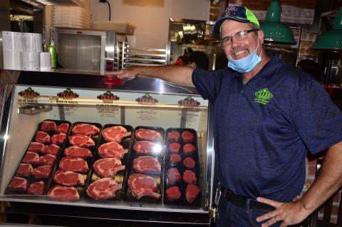 Steve Hale, managing partner for the Lake City Texas Roadhouse, poses alongside an assortment of meats ahead of the opening of the chain’s new location. (CARL MCKINNEY/Lake City Reporter)