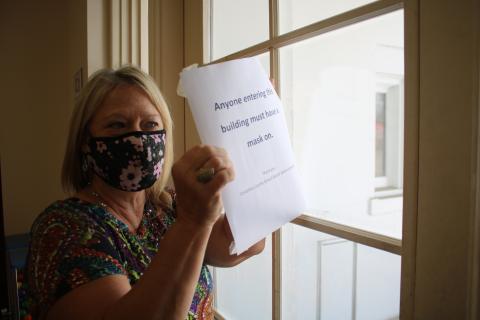 Marsha Wallace, Columbia County School Board office information specialist, places a sign on the central office’s door notifying the general public they must wear masks before entering the building. (TONY BRITT/Lake City Reporter)