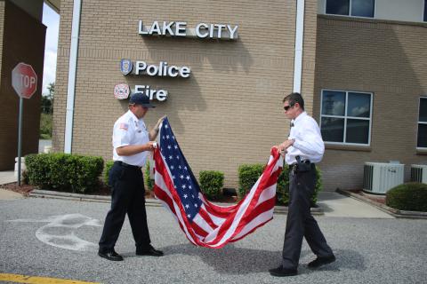 Josh Wehinger, (from left) Lake City Fire Department assistant chief and Andy Mangrum, a Lake City Police Department investigator, fold the American Flag after a brief 9/11 memorial ceremony rehearsal Wednesday afternoon at the city’s Public Safety building. (TONY BRITT/Lake City Reporter)