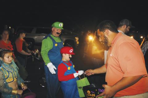 Robert Stalvey and Hagan Stalvey, 7, came dressed as Luigi and Mario at last year’s Trunk or Treat. Here Hagan accepts candy from Steven Flores. (FILE)