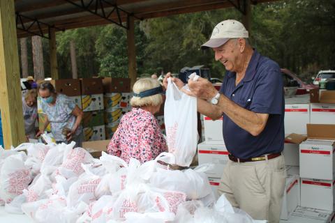 Bud Parker works on tying a plastic bag as he and other volunteers at Lake City Church of Christ distribute food and other commodities Thursday afternoon. More than 200 vehicles passed through the event collecting bags and boxes of food. (TONY BRITT/Lake City Reporter)