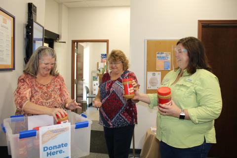 Julia Fulton (from left), county extension service secretary specialist, gets jars of peanut butter from Garnet Dasher, county extension service secretary specialist, and Heather Janney, UF/IFAS Extension Columbia County Extension director and 4H agent, on Tuesday afternoon as they collect peanut butter for the Peanut Butter Challenge. (TONY BRITT/Lake City Reporter)