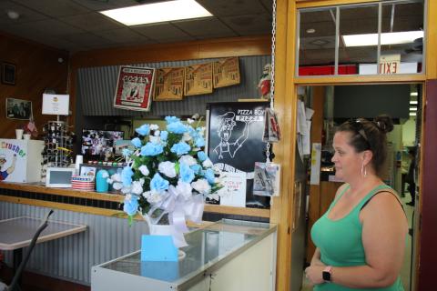 Caryn Cooper, daughter of the late Robert Warren Cooper Jr., who was the owner of the Pizza Boy Pizza restaurant, looks at a bouquet of flowers on the restaurant’s counter Wednesday afternoon. (TONY BRITT/Lake City Reporter)