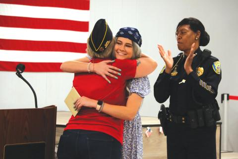 Taylor Sapp (middle) hugs 3rd Vice Commander of American Legion Post 57 Victoria Ziegler as Lake City Police Chief Argatha Gilmore offers applause Tuesday night. (MORGAN MCMULLEN)
