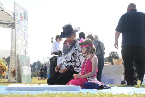 Dulcinea Strube (left) teaches 7-year-old Olivia Carr how to play jacks near the Woman’s Club setup Saturday during Founder’s Day celebrations. (MORGAN MCMULLEN/Lake City Reporter)