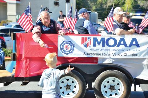 A member of the Military Officers Association of America hands a flag to a child during the 2019 Veterans Day Parade in Lake City. (FILE)