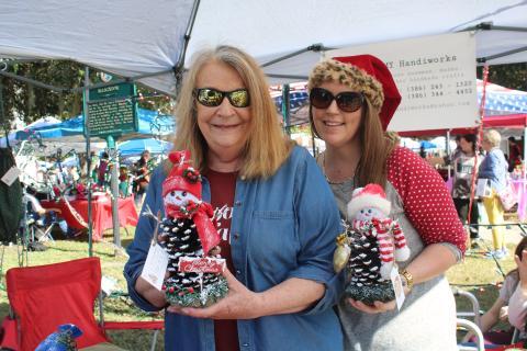Janice Medford (left) and Jaime Brock show off snowmen made out of pinecones at a vendor’s booth on Saturday. (TONY BRITT/Lake City Reporter)