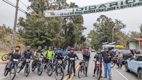 Bikers participating in the 2022 IDIDARIDE pose underneath a banner marking the event. More than 300 participants rode through the off-road courses set up for the 50-mile challenge. (COURTESY)