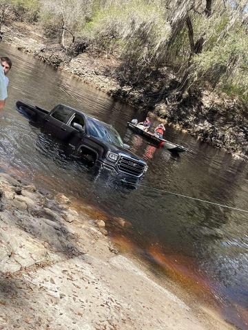 A black GMC truck gets a tow out of the Suwannee River Saturday afternoon after it rolled into the water. (COURTESY)