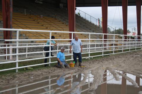 Dale Brown (middle) and Terry Hayes get muddy while working on verifying stakes that will be used for timers during the 28th Aannual Florida Gateway Pro Rodeo in the Florida Gateway Fairgrounds Rodeo Arena on Thursday afternoon. Kylee Brown (left) looks on. (TONY BRITT/Lake City Reporter)
