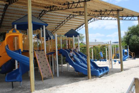 Cody Pritchard Jr. (from left), 6, and his sisters Graesyn Pritchard, 5, and Londyn Pritchard, 7, take a ride down the slides at Kiwanis Park on Friday afternoon. A shade structure was recently added to the park. (TONY BRITT/Lake City Reporter)