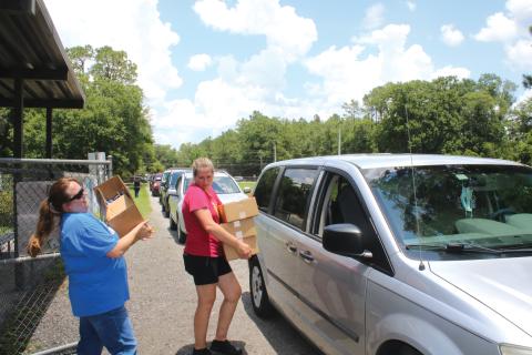 Alicia Blackford (from left) and Laurie Renegar carry meals to a minivan at Five Points Elementary School last summer. (FILE)