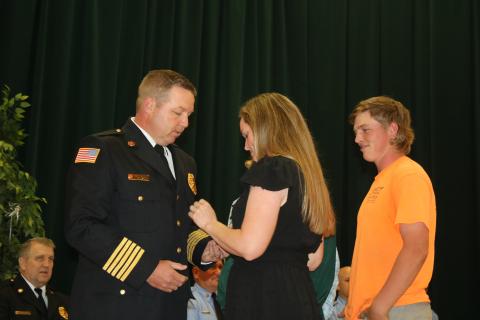 Lake City Fire Chief Josh Wehinger receives his badge from wife, Lari, as son, Ty, looks on during a swearing-in ceremony Tuesday night at the Columbia County School District Administrative Complex Auditorium. (TONY BRITT/Lake City Reporter)