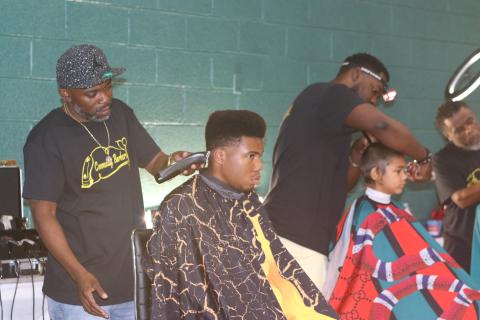 Tyrone Mullins (standing), an organizer for the Community Barbers Giving Back event, works as one of 11 barbers on Sunday that provided free haircuts at the back to school event. (TONY BRITT/Lake City Reporter)