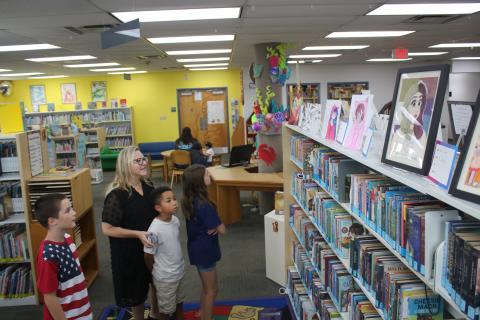 Tracy Mitchell (black dress), Alexander Mitchell, 8, (gray shirt), Isaac Gollery, 10, (red/white/blue shirt) and Audrey Mitchell, 10, (blue shirt) look at youth-submitted art pieces in the Columbia County Public Library on Thursday afternoon. The pieces, which will be on display at the library throughout September, are pieces that were submitted for the Third Annual Columbia County Public Library Youth Art Contest. (TONY BRITT/Lake City Reporter)