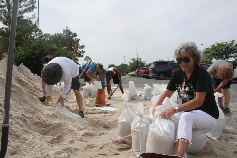 Lila Pasternak sits on sandbags in the Southside Sports Complex on Tuesday morning while tying other sandbags. The county public works department placed several piles of sand in the parking lot allowing residents to fill the bags or get aid from others at the site, which will be open from 7 a.m.-7 p.m. today. (TONY BRITT/Lake City Reporter)