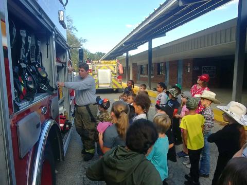 Bryan Govantes (far left), a Columbia County Fire Rescue firefighter, shows Columbia City Elementary School second grade students the equipment that firefighters use during a Fire Prevention Week presentation on Thursday morning. (TONY BRITT/Lake City Reporter)