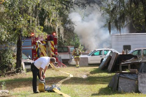 Dwight Boozer, Assistant Fire Chief of the Lake City Fire Department, looks over this shoulder while coupling hoses as a firefighter heads toward the blaze in the background. (TONY BRITT/Lake City Reporter)