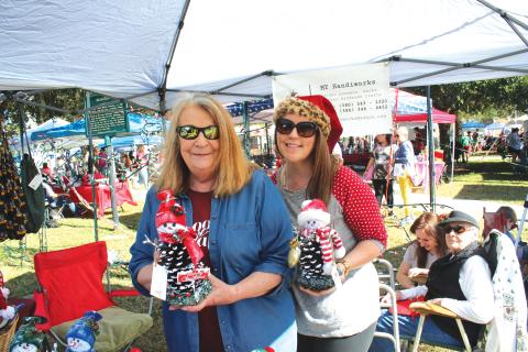 Janice Medford (left) and Jaime Brock show off snowmen made out of pinecones at a vendor’s booth during last year’s holiday market. (FILE)