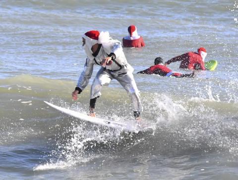 Surfer Corey Howell in a space man Surfing Santa suit, rides with waves with other surfing Santas for the 14th annual Surfing Santas of Cocoa Beach event Christmas Eve morning, Saturday, Dec. 24, 2022. Cold temperatures in the 30s Fahrenheit thinned out the surfers, but thousands showed up for the annual holiday event that benefits the Florida Surf Museum and Grind for Life, a local charity benefiting people with cancer. (MALCOLM DENEMARK/Florida Today via AP)