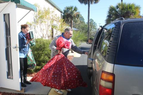 JD Curls prepares to load a bag of toys into a vehicle as Jennifer Davis brings a handful books and other items to the vehicle during the Christmas basket dispersal Monday morning at the Christian Service Center. (TONY BRITT/Lake City Reporter)