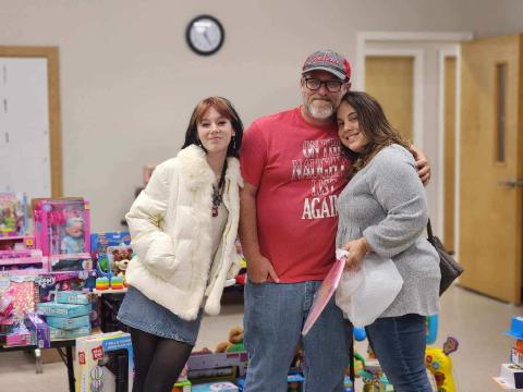 Kids Feeding Kids officials Emily Cole (from left), John Cole and Sharon Simpkins share a group hug during the organization’s ‘Miracle on KFK Street’ on Saturday night. (COURTESY)