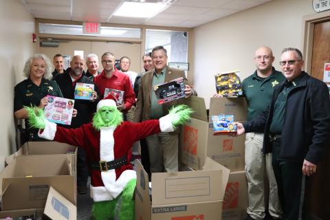 Eddie Medina, dressed as the Grinch, shows off the donated toys in front of Sheriff Mark Hunter (center) Wednesday morning at the Columbia County Sheriff’s Office. (COURTESY)
